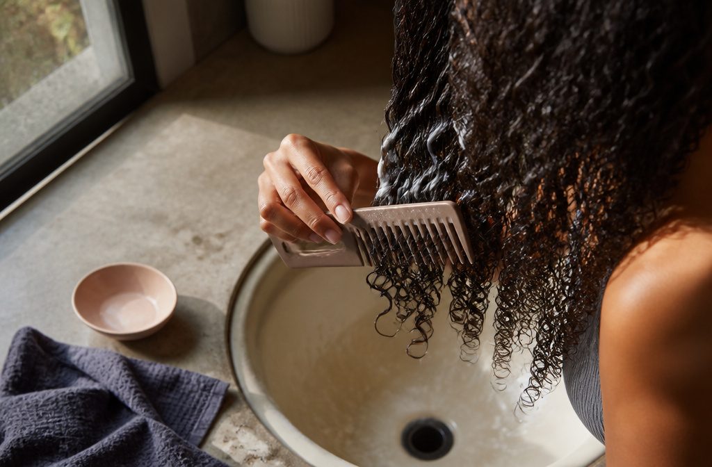 Curly-haired woman applying conditioner to one section of her hair