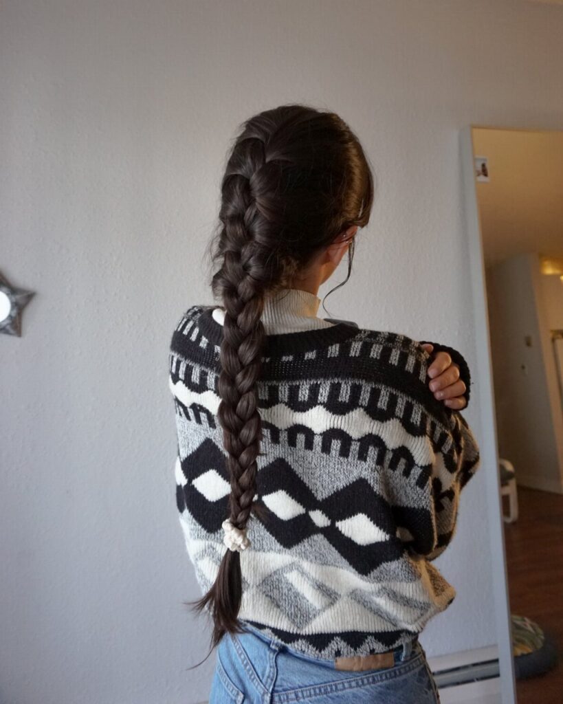 Long dark French braid hanging down the back of a person in a patterned sweater