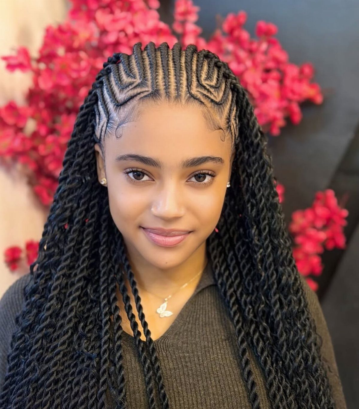 Young woman displaying long braids and geometric cornrows against pink flowers
