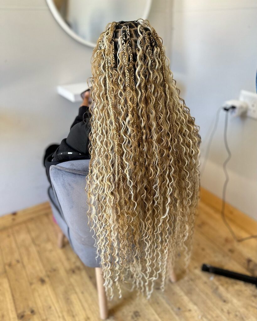Long honey-blonde braids with loose curls cascade down a seated person's back.