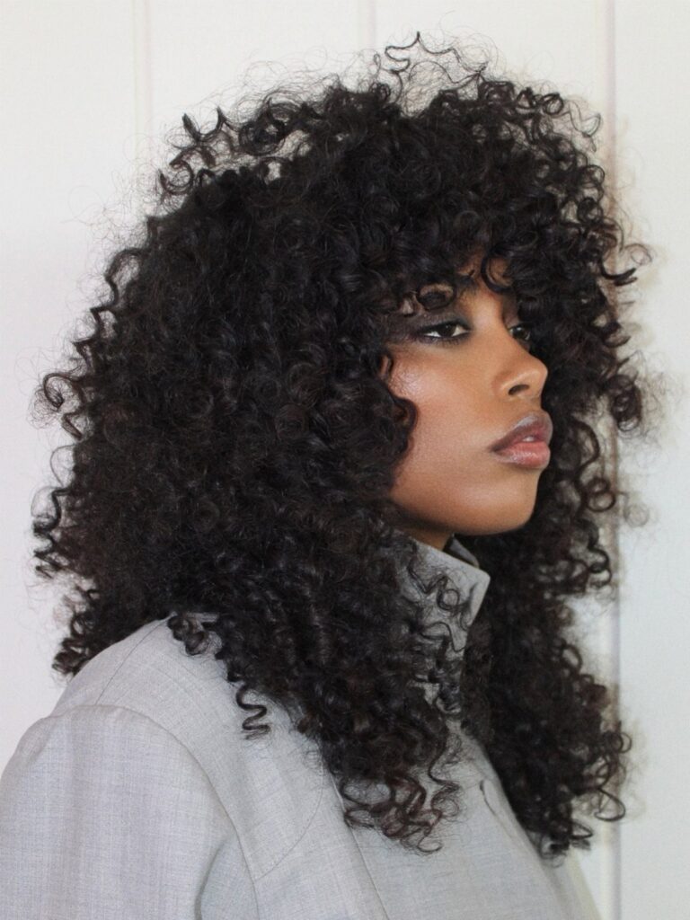 Voluminous dark curls form a rounded layered shape around the person's face