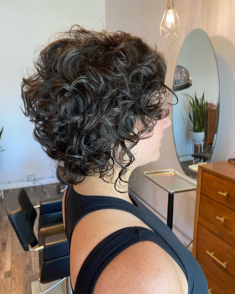Layered dark curls frame a woman's face in a salon