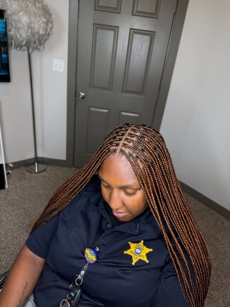 Small box braids fall over a seated woman’s shoulders in a room