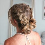 Loose double braids gathered into a messy low side bun on light brown hair